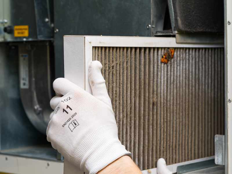 Dirty HVAC filter causing foul smell in living room, technician preparing to replace and clean the system.